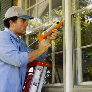 Man sealing a window gap with caulk